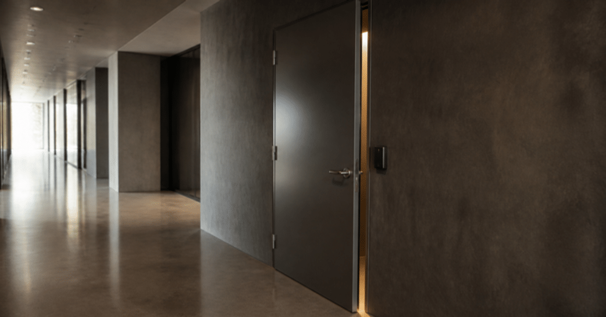 Steel door left slightly ajar in an empty office corridor, light spilling from the gap